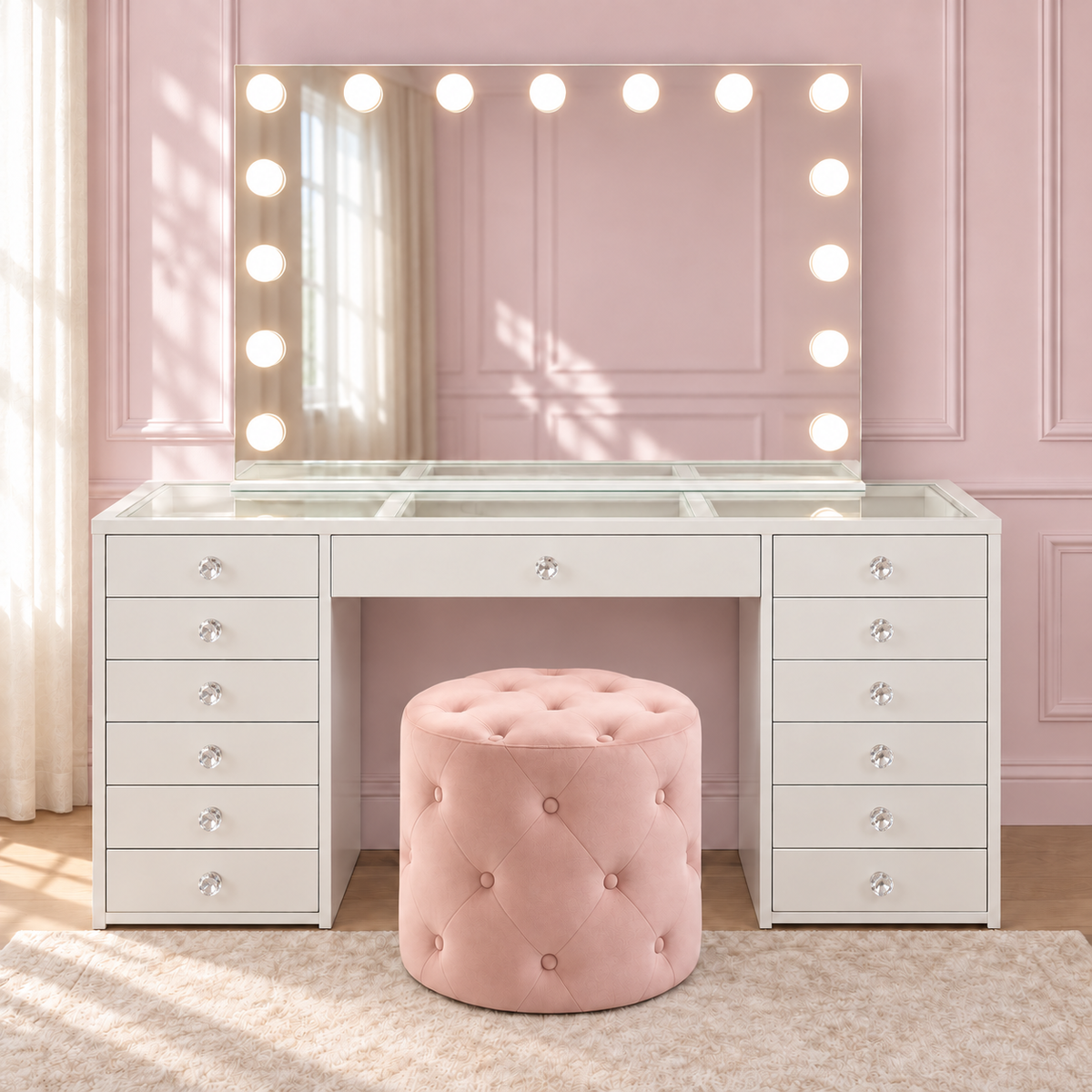 Essentials Collection Babyface Edition white glass-top vanity, illuminated bulb mirror and pink tufted ottoman — with clear faceted crystal drawer knobs.