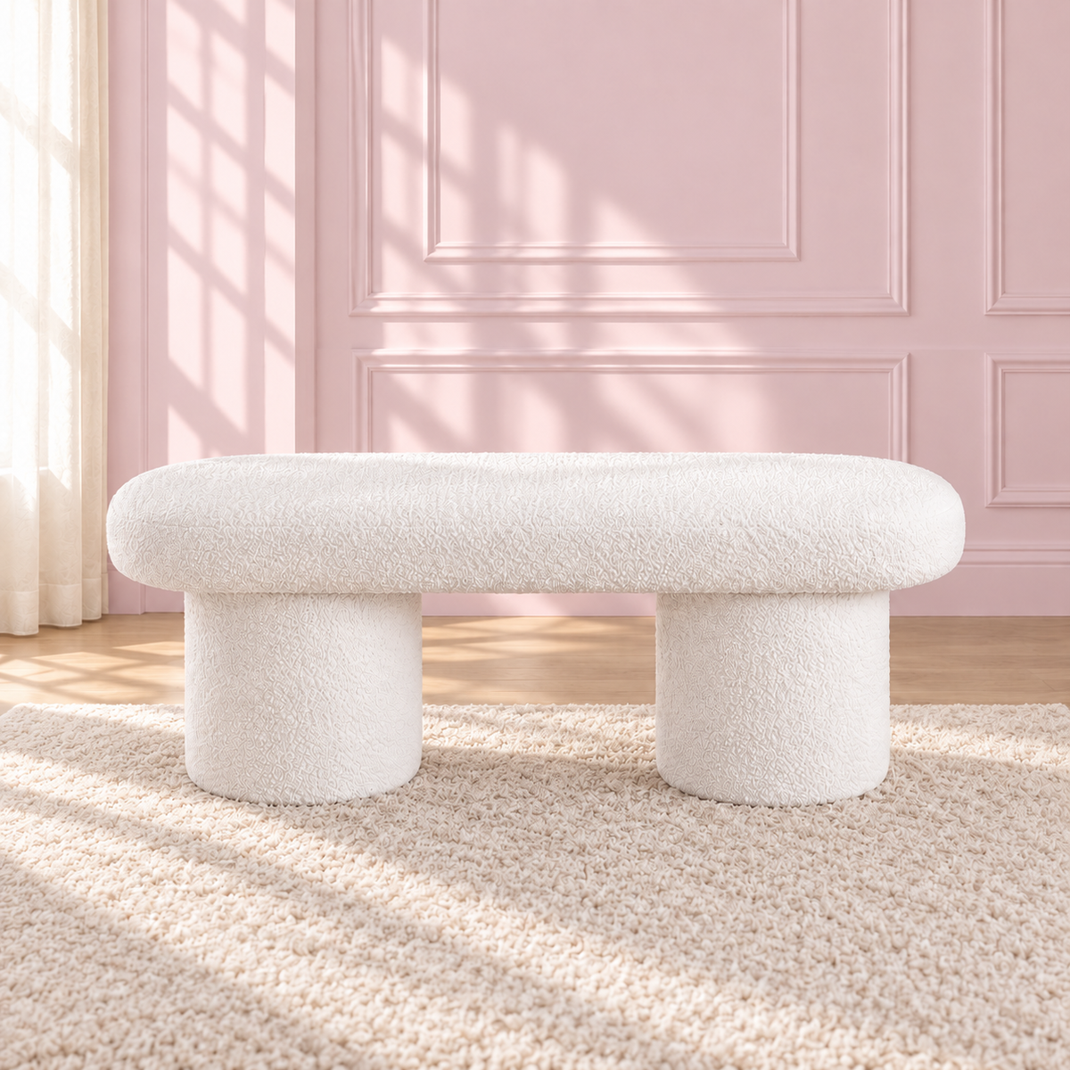 Liora white upholstered bench with a rounded seat and two cylindrical legs against a pink wall.