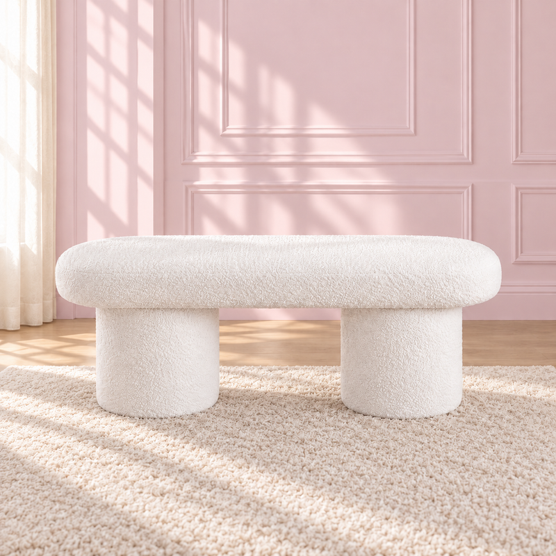 Liora white upholstered bench with a rounded seat and two cylindrical legs against a pink wall.