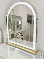 Mini Aries 100 x 80 cm gold makeup mirror with illuminated arched LED border and gold base in the showroom