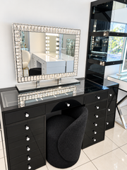 Mini Dollface Black Edition glass-top vanity with crystal drawer knobs, shown in the showroom with a crystal-framed makeup mirror and black seat.
