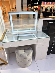 Mini Nova illuminated mirror on a Mini Deluxe glass-top vanity with a grey Marshmellow Ottoman in the showroom