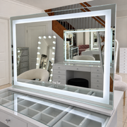 Nova makeup mirror with illuminated rectangular LED border on a glass-top vanity in the Vanity Vault showroom