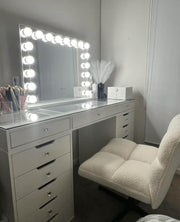 Seraphina illuminated mirror on a white glass-top vanity with a cream swivel chair.