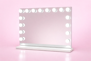 Seraphina Hollywood mirror with illuminated bulbs displayed above a white vanity in a pink showroom.